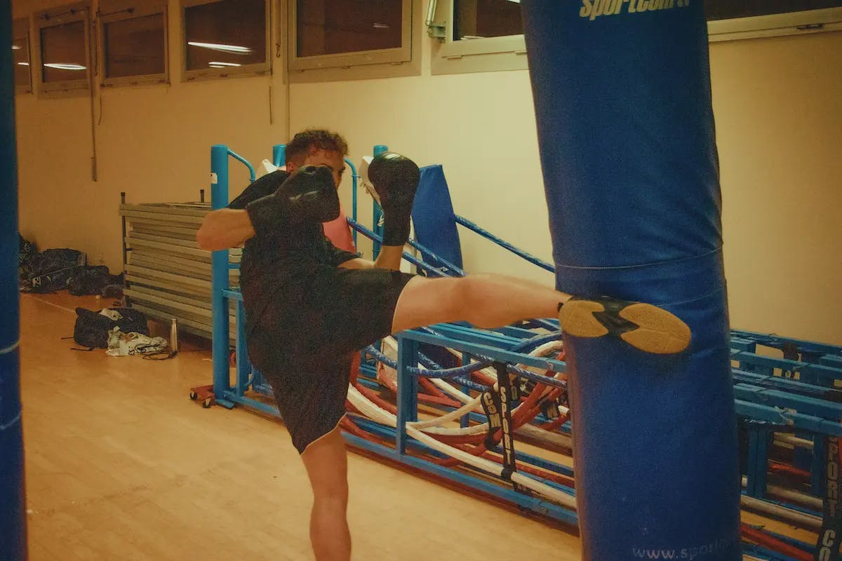 Photographie d’un adhérent du club de boxe en plein entraînement, frappant dans un sac de frappe avec son pied.