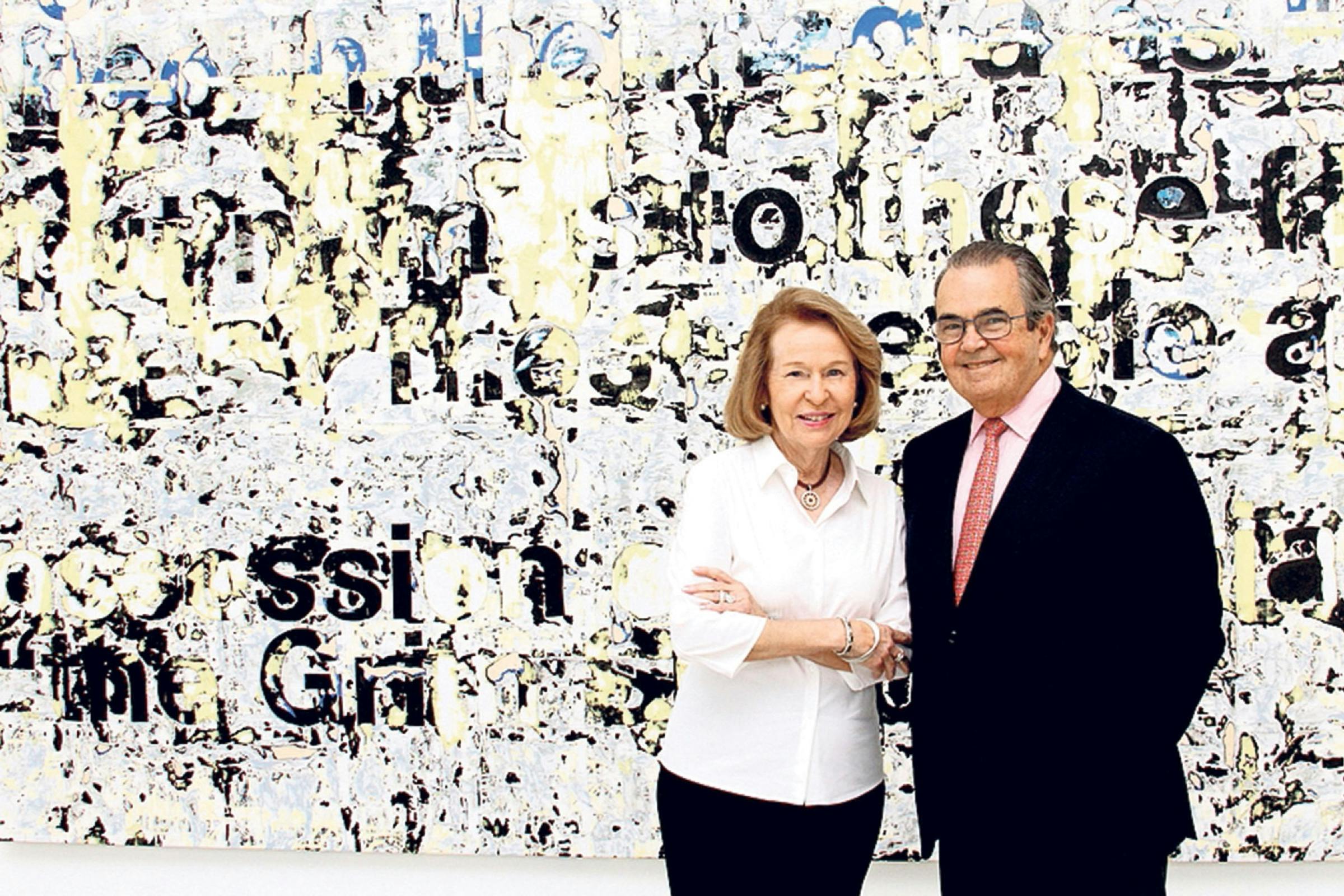 A photo of Rosa and Carlos de la Cruz in front of a painting by Mark Bradford.