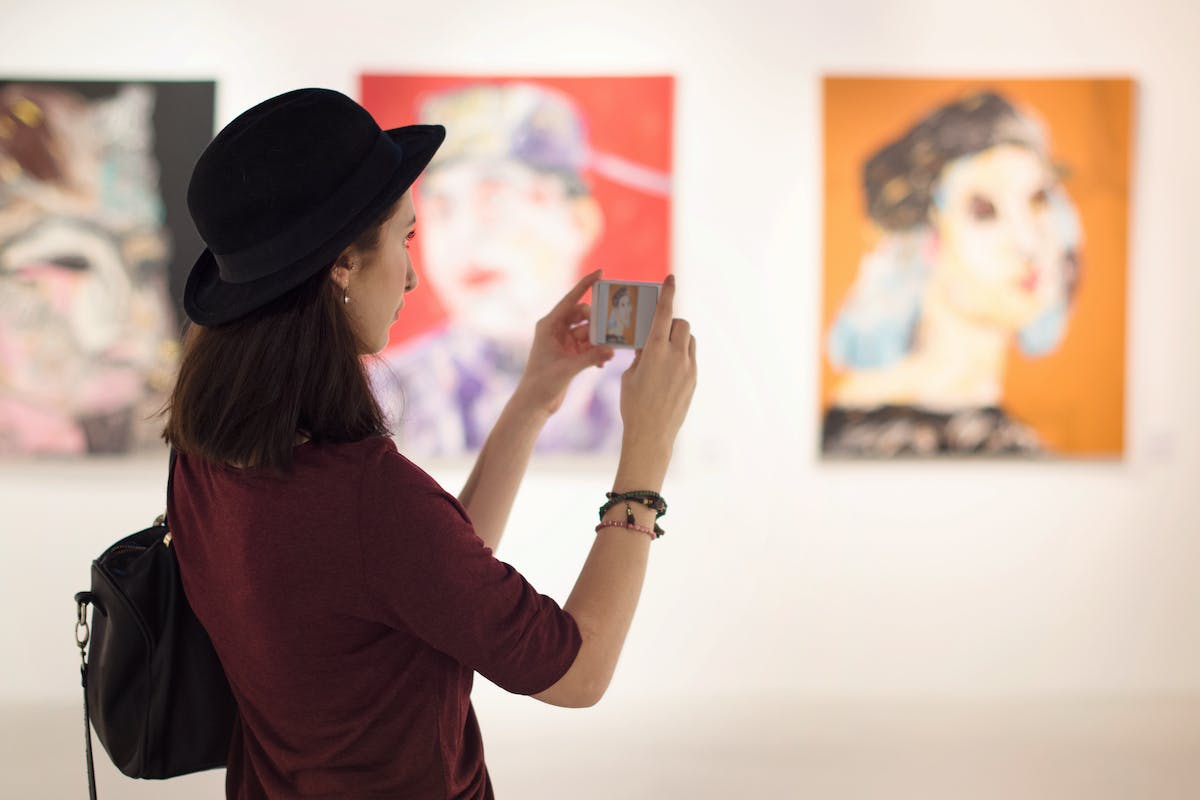 A woman taking photos of artwork on her cellphone.