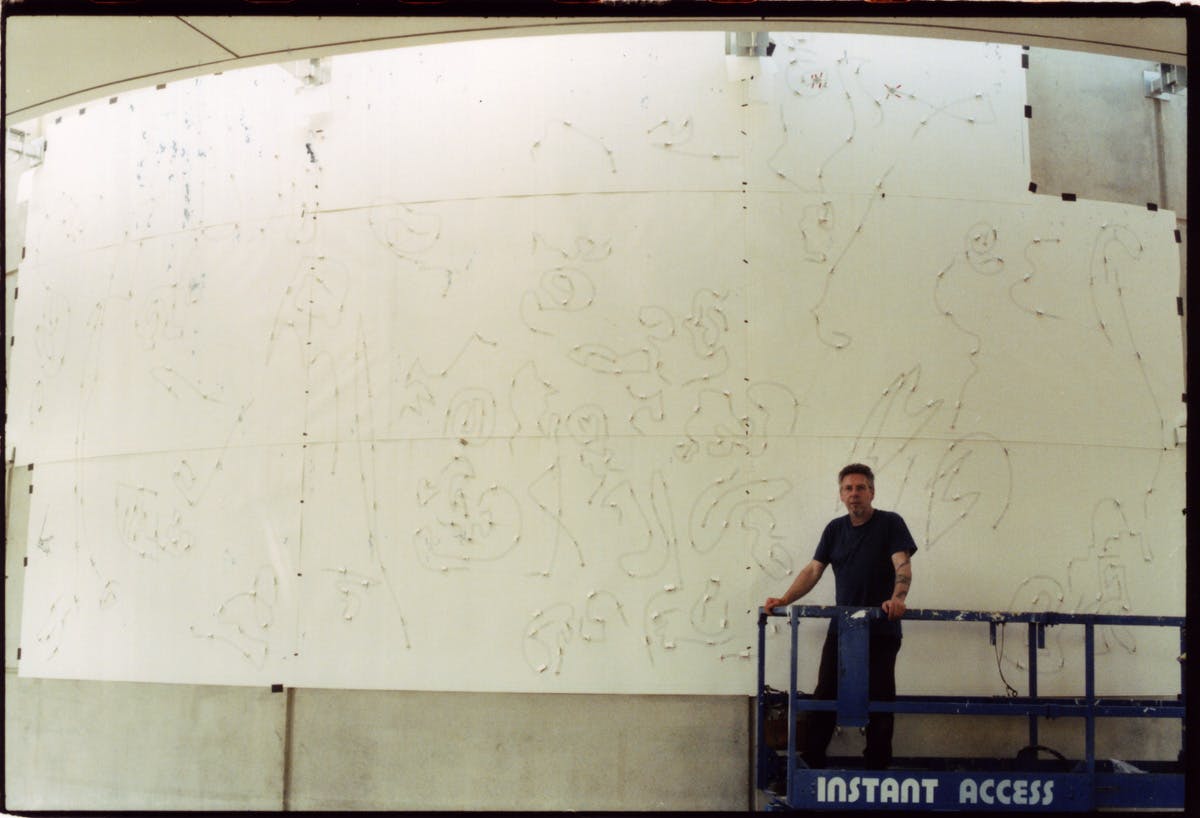 The artist on a scissor-lift as he maps out the placement of each neon tube, 2003. 