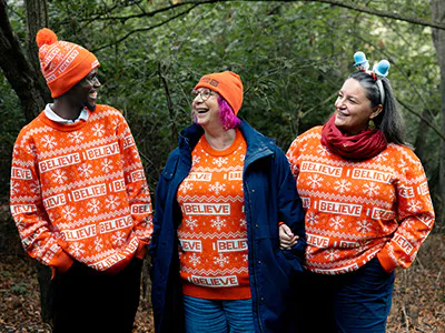 Three adults smiling in the woods, wearing Alzheimer's Research UK festive jumpers. 