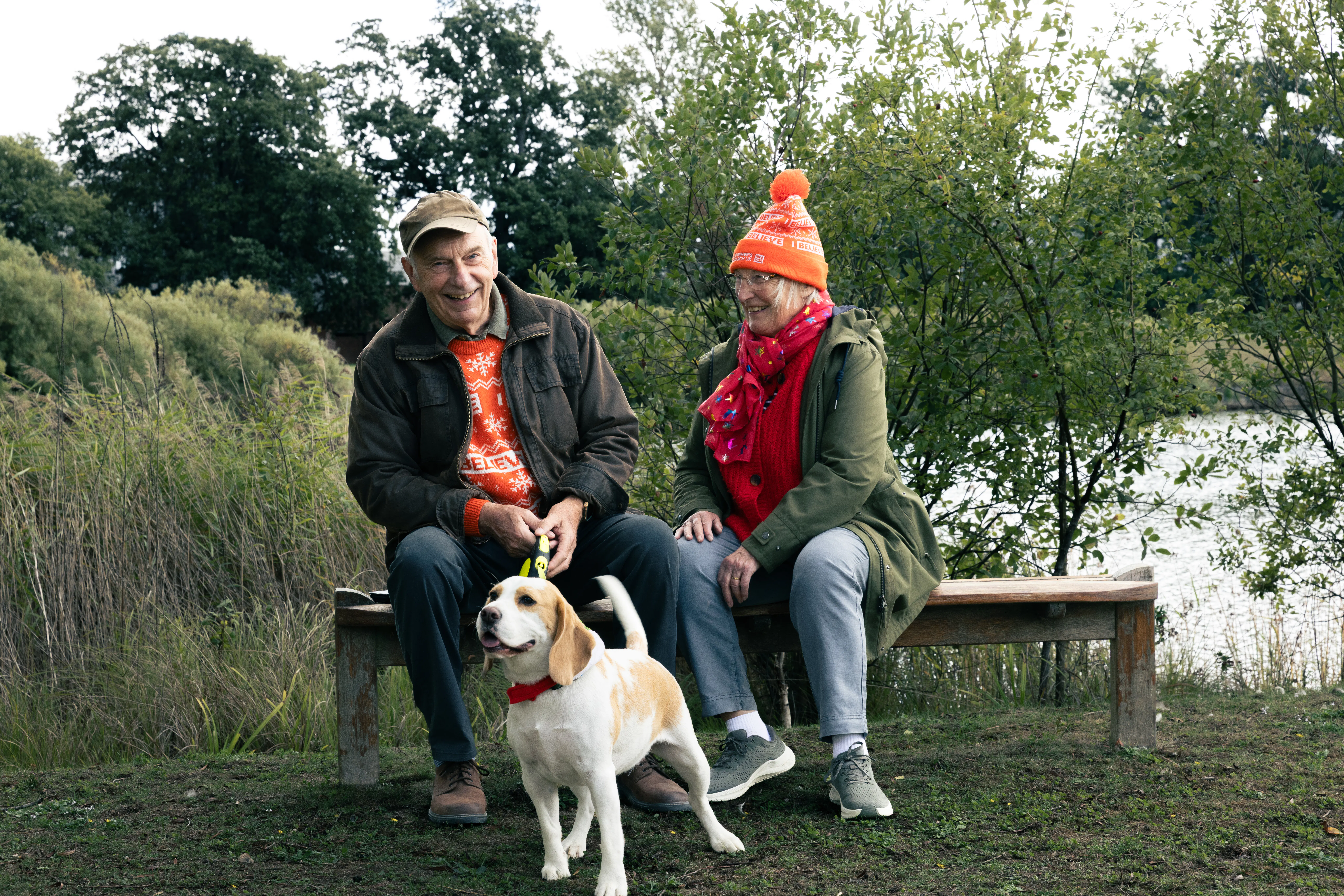 Alzheimer's Research UK supporters wearing ARUK festive jumpers and hats in the park with a dog.