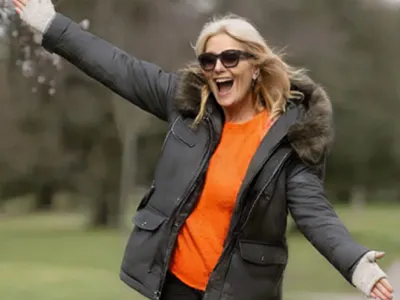 A celebrity smiling with arms outstretched wearing an Alzheimer's Research UK jumper.