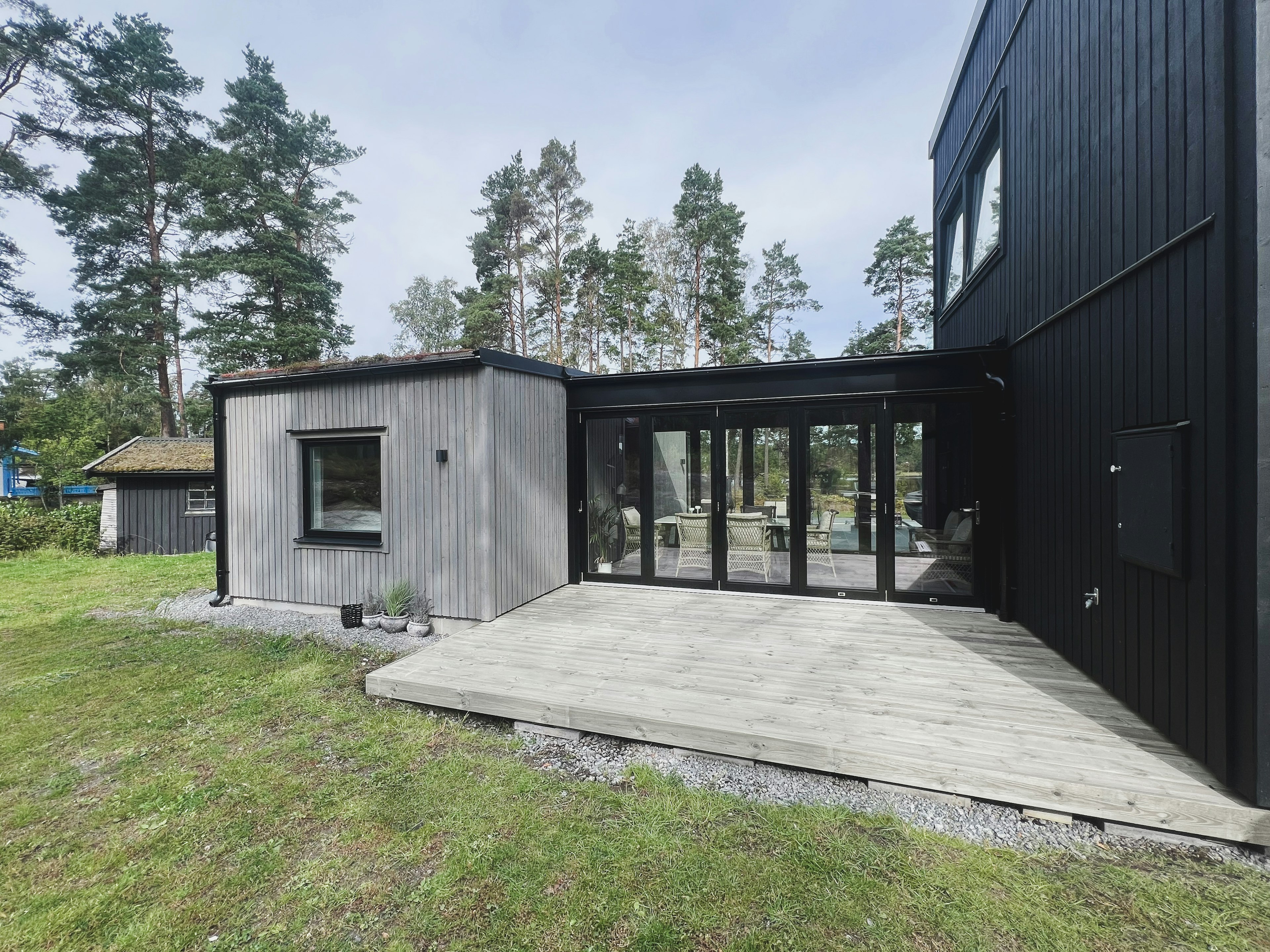 Exteriör vy av glasad gång som förbinder gästhus med huvudbyggnaden, arkitekt ritade hus i modern stil.