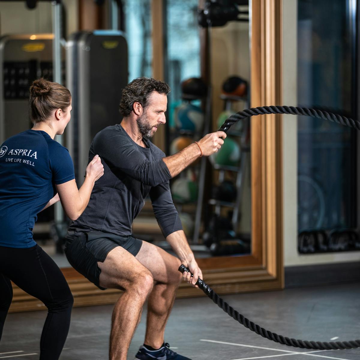 Man with a female personal trainer holding battle ropes 