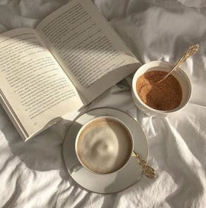 Livre et tasse de café posés sur une couette Atelier Unes