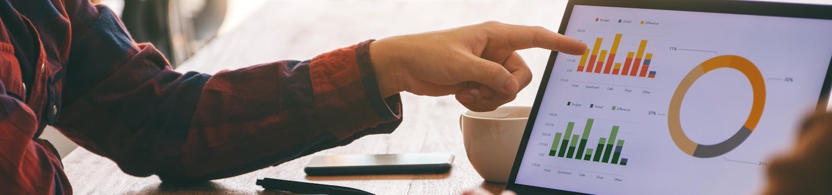 Kobieta wskazująca palcem na laptopa, na którego ekranie widać aplikację do prezentowania danych, wykresy