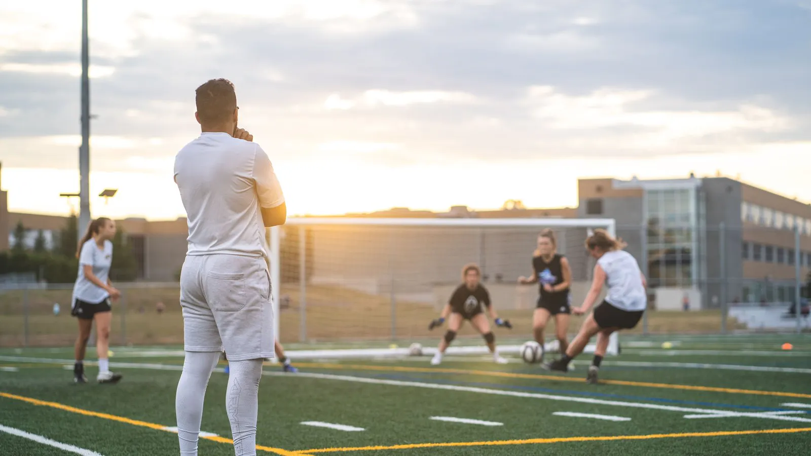 Coach watching a shooting drill from the sideline in the evening light