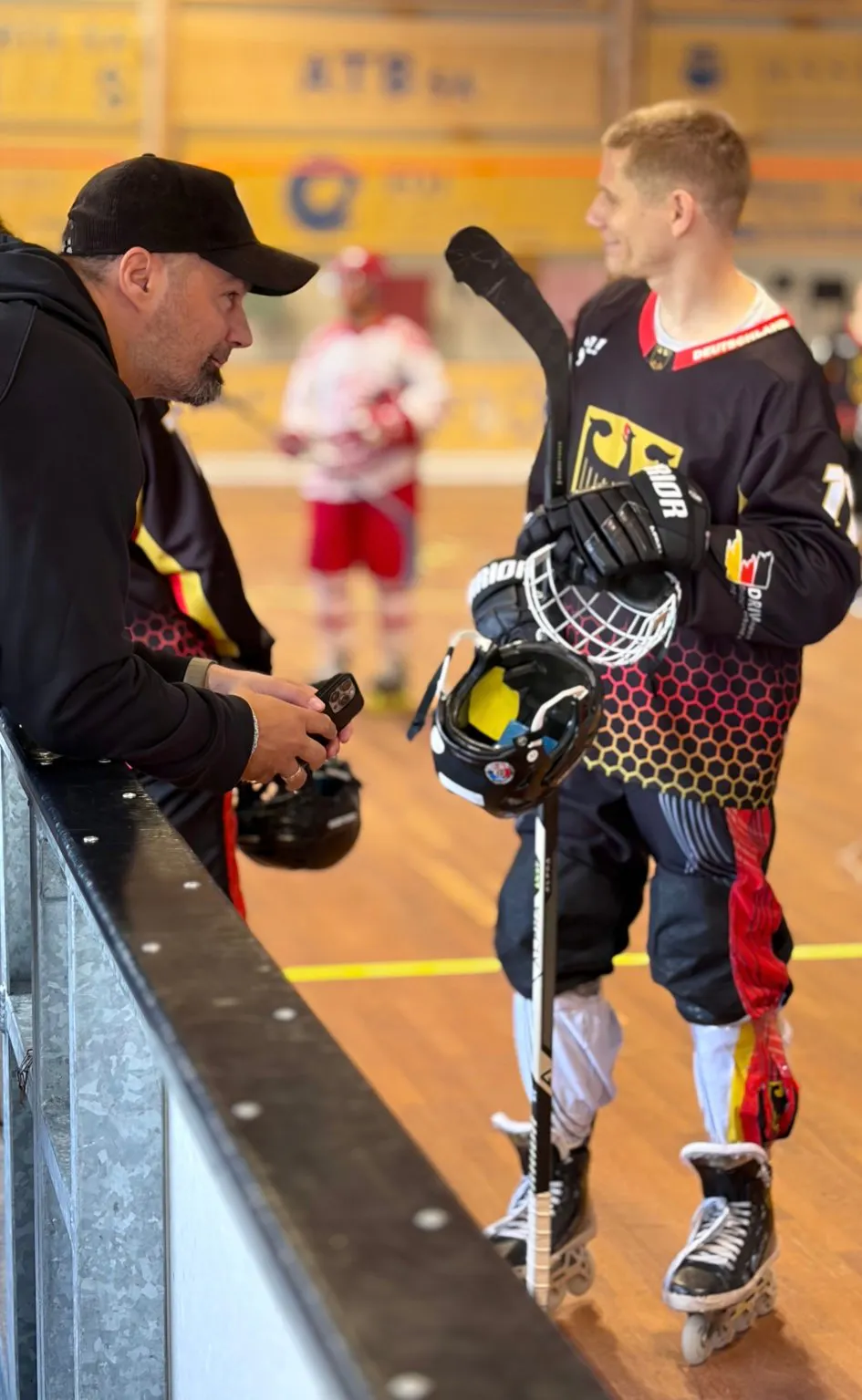 Trainer der deutschen Inline-Skaterhockey-Nationalmannschaft im Gespräch mit einem Spieler an der Bande