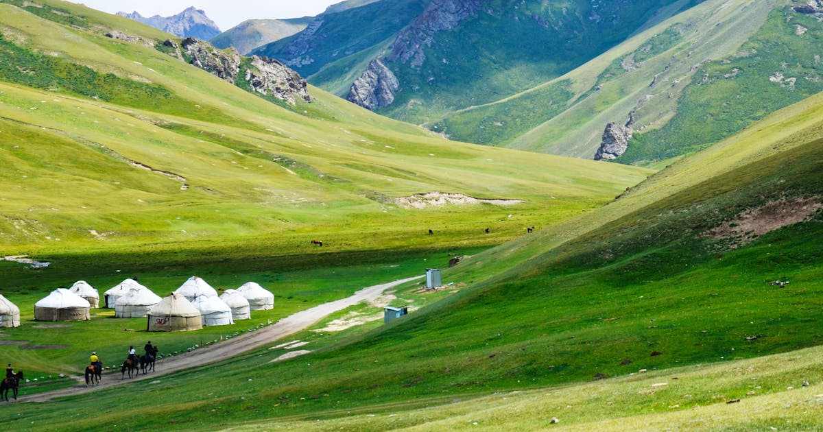 Green Kyrgyzstan landscape, including mountains in the background and traditional Kyrgyzstan tents.