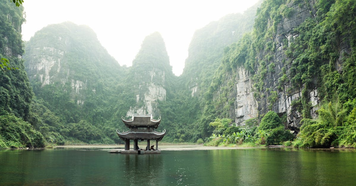 Traditional building surrounded by a body of water and a rocky mountain.