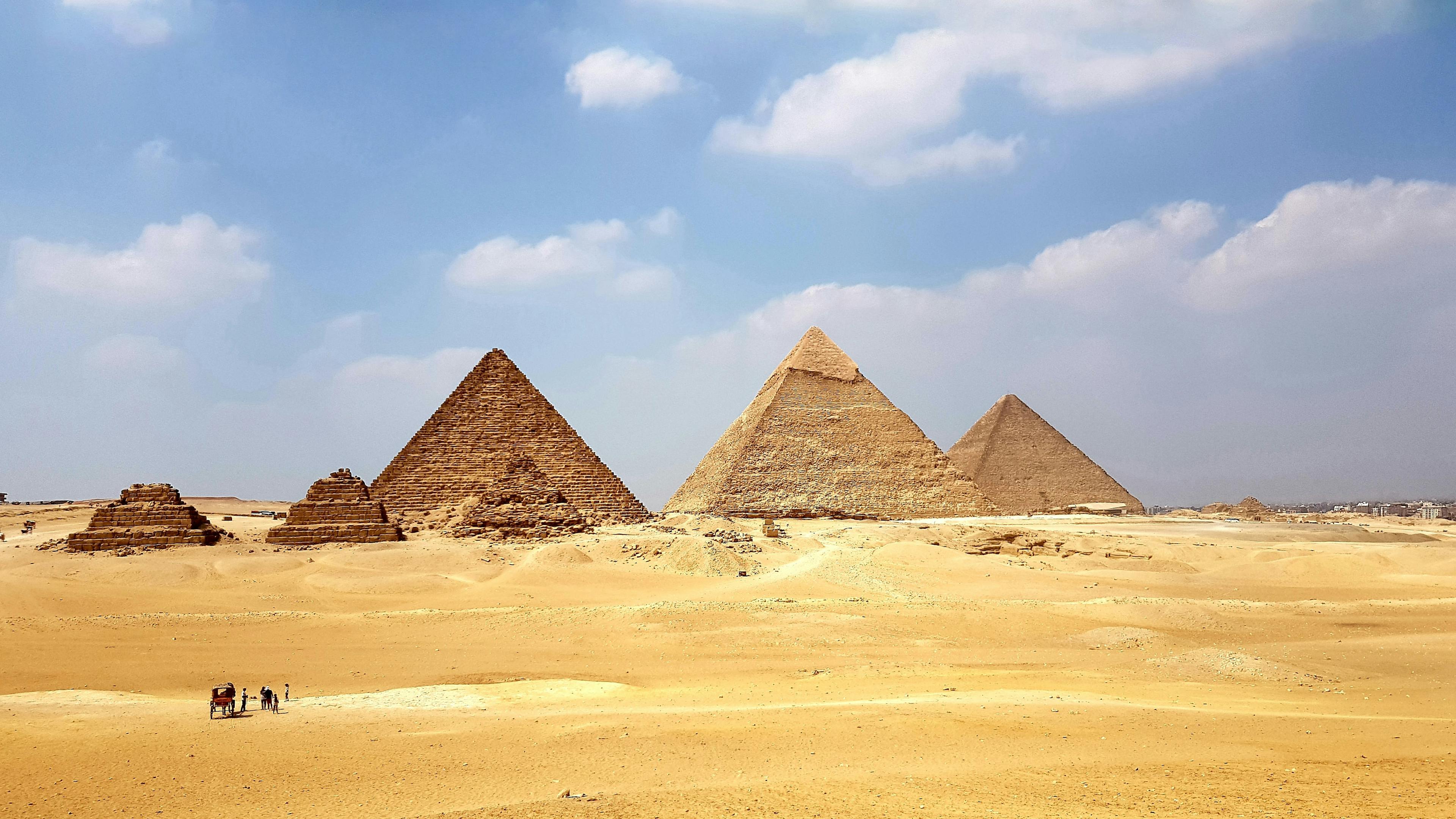 The great pyramids of Egypt during the day time from afar. A small group of people walking with a caravan.