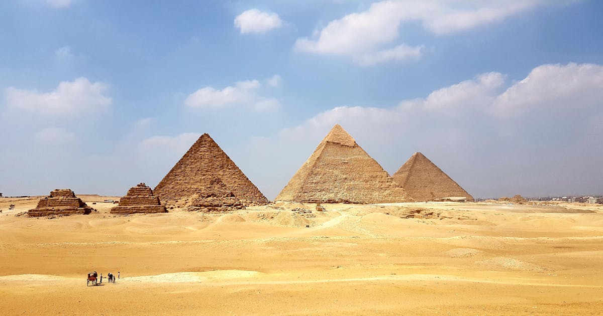 The great pyramids of Egypt during the day time from afar. A small group of people walking with a caravan.