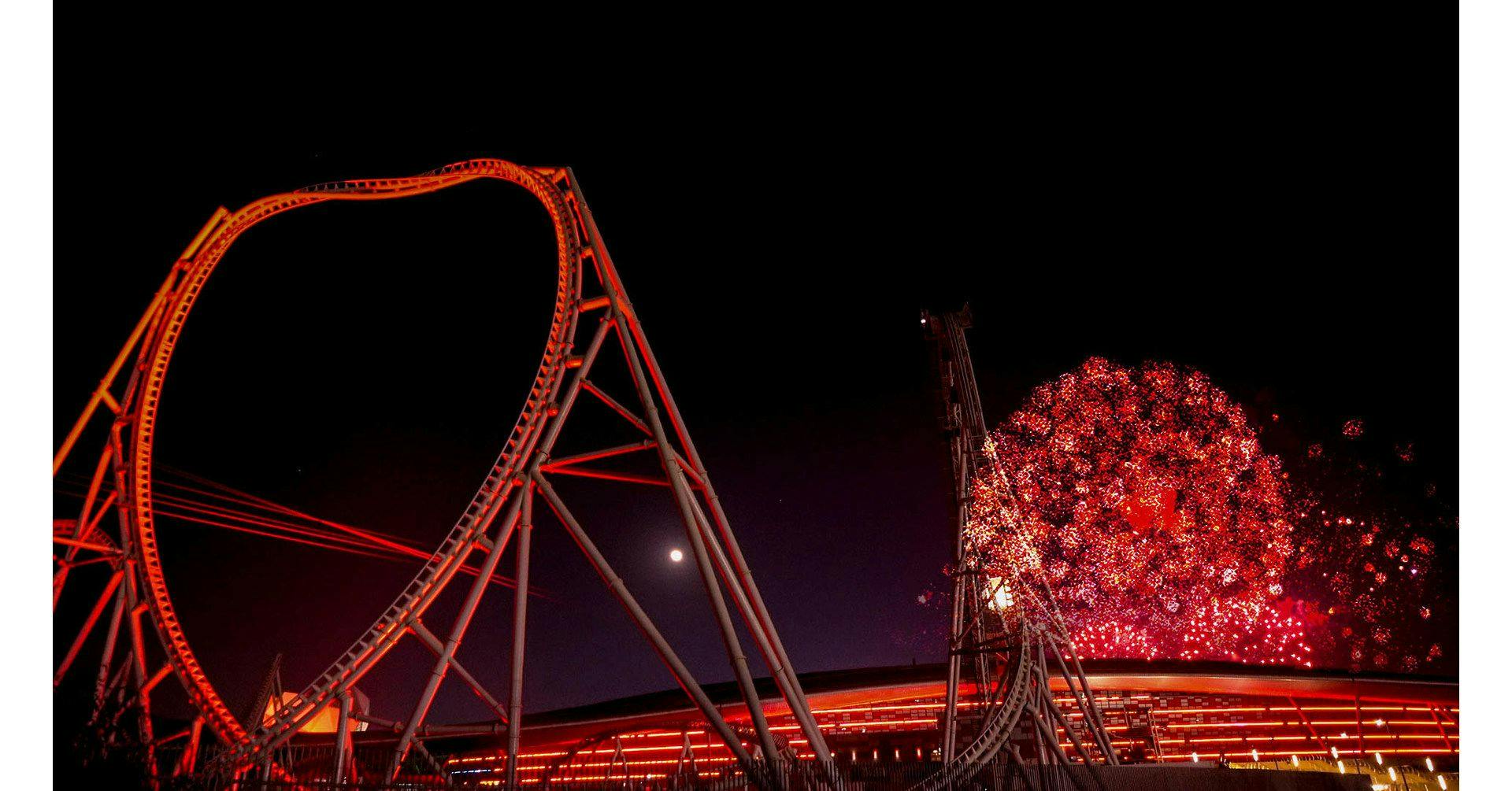 A roller coaster structure reflecting red light during nightime.