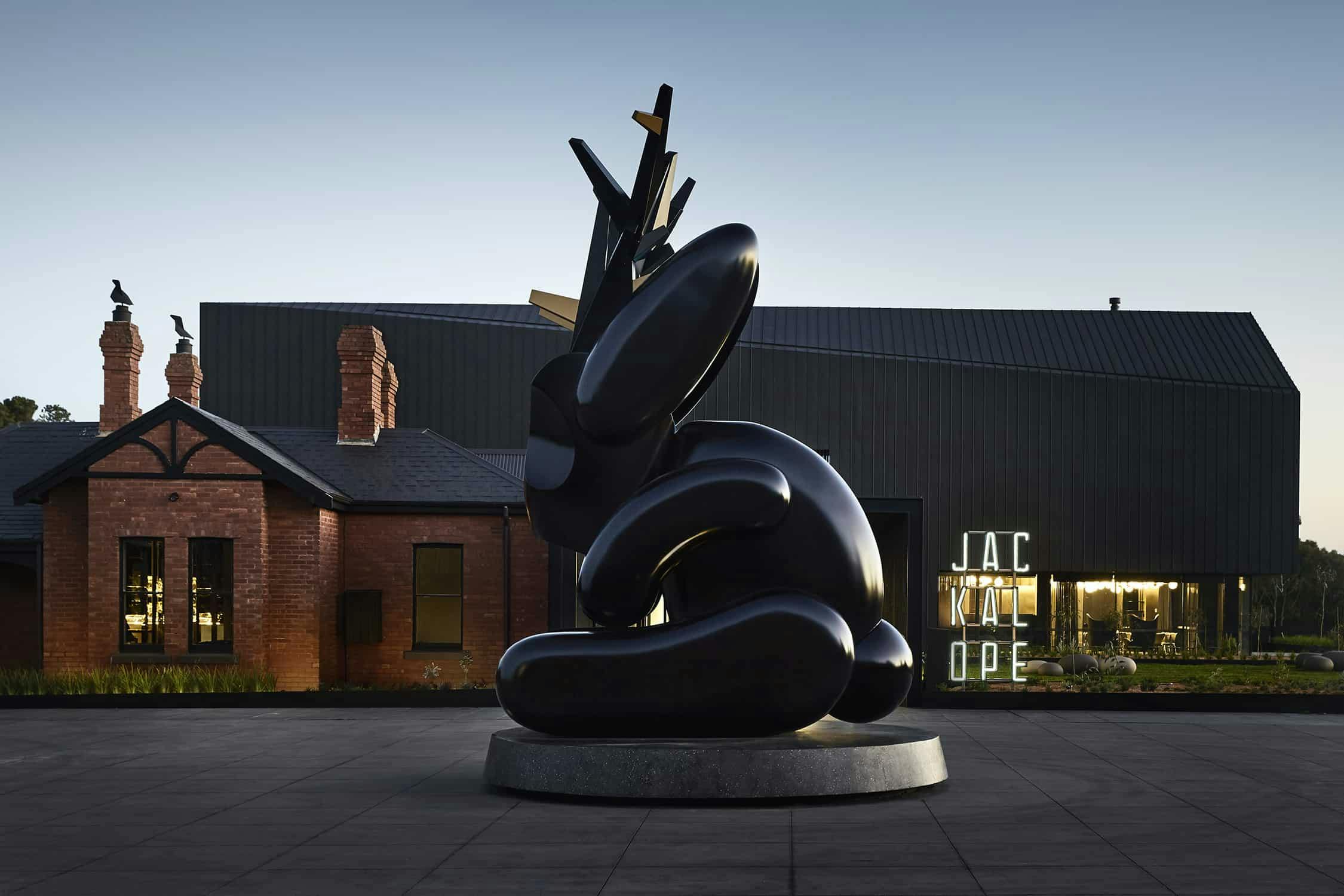 An artistic black statue with a black and brown house in the background.