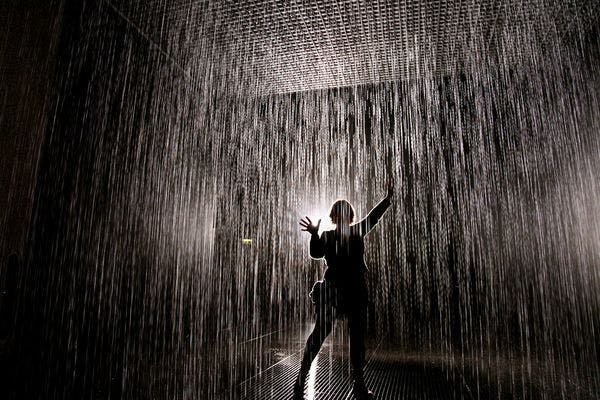 A dark photo of a person standing in a room while water is falls from the ceiling.