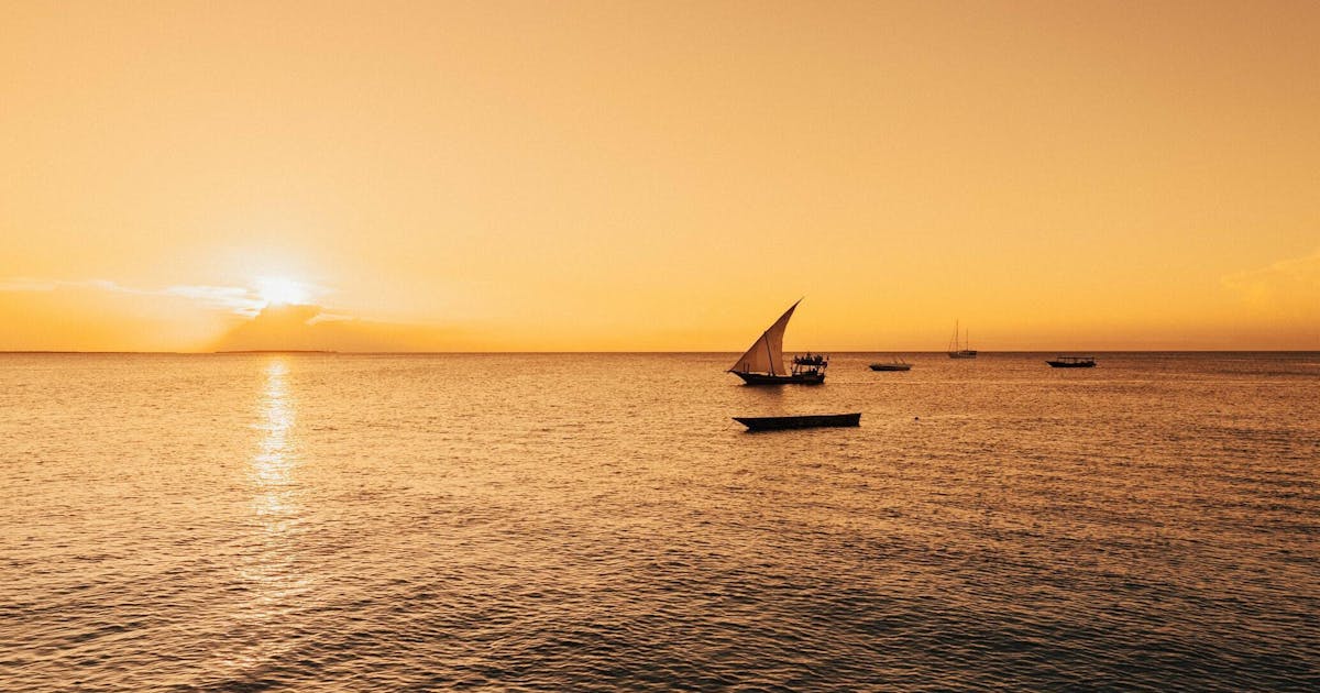 View of a sail boat drifting on the ocean during a bright orange sunset