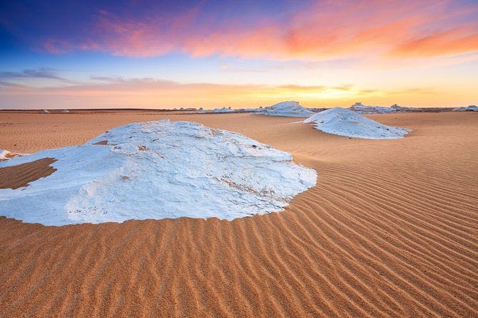 A desert with white stone-like structures and a colorful sky.