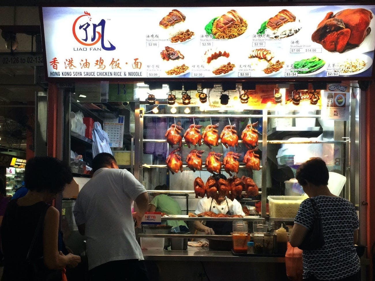 People standing infront of a Thai street food shop serving chicken.