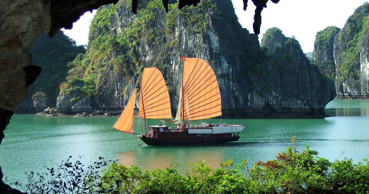 Vietnamese boat floating on blue water surrounded by rocks and greenery during daytime