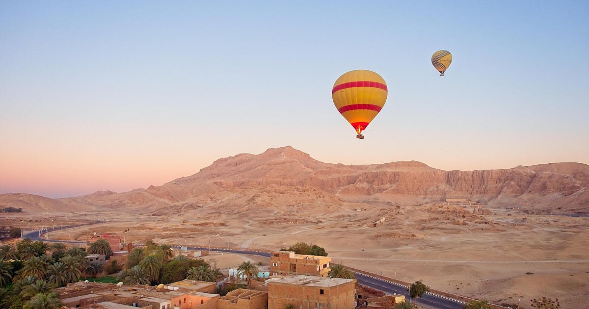 A beautiful view of yellow and red hot air balloons floating above a dessert during sunset.
