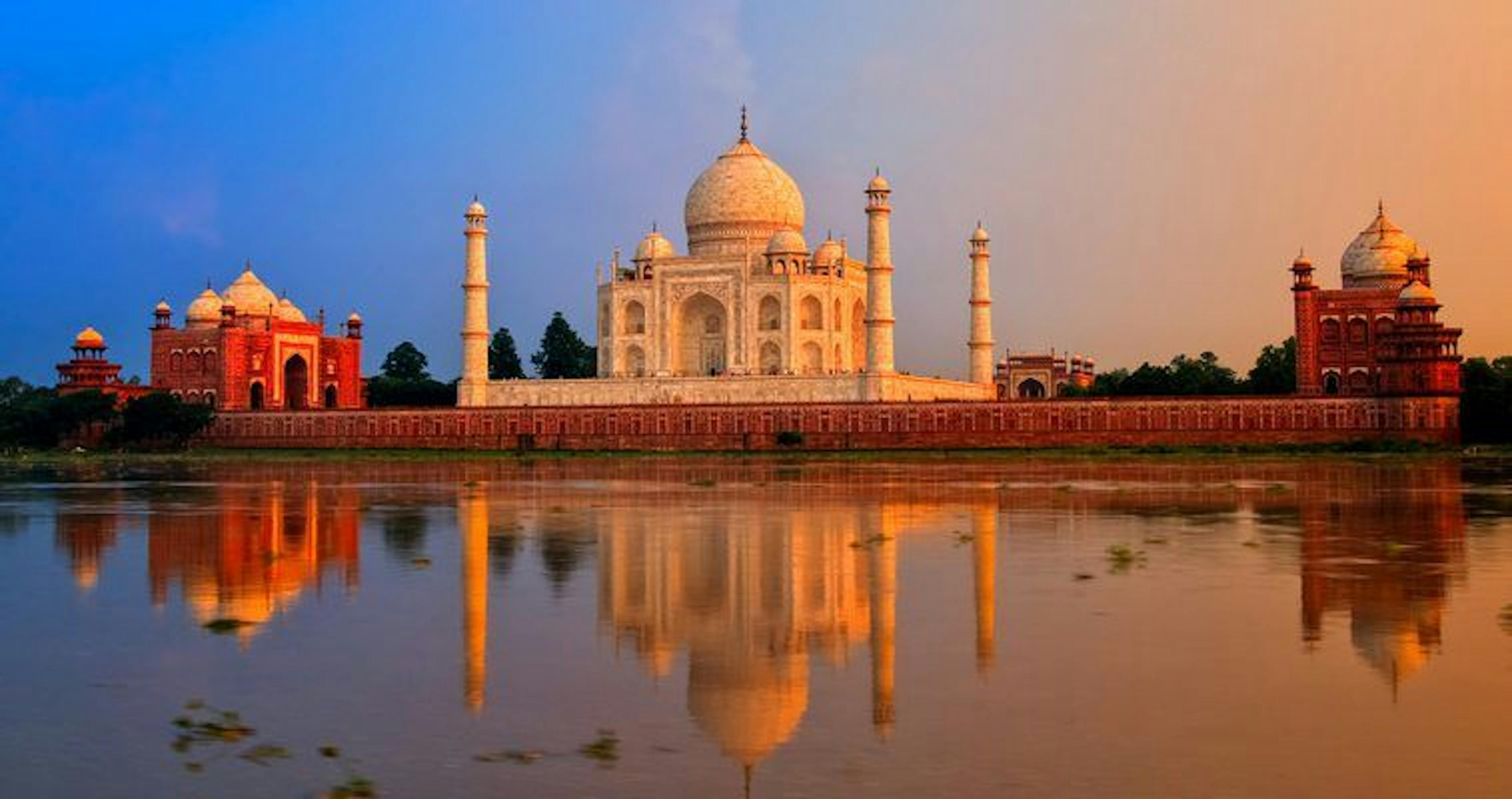 A white temple reflectiing from a body of water with a blue and orange sky.