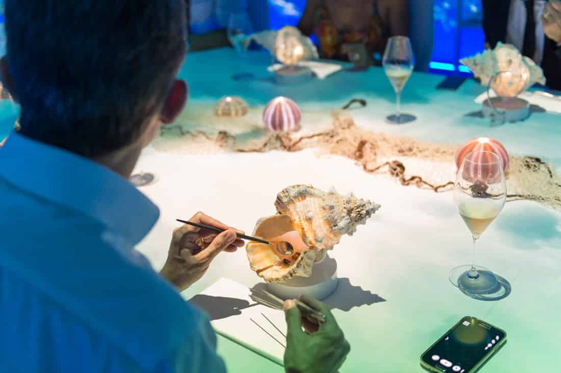 People around a table while eating a dish from a shell.