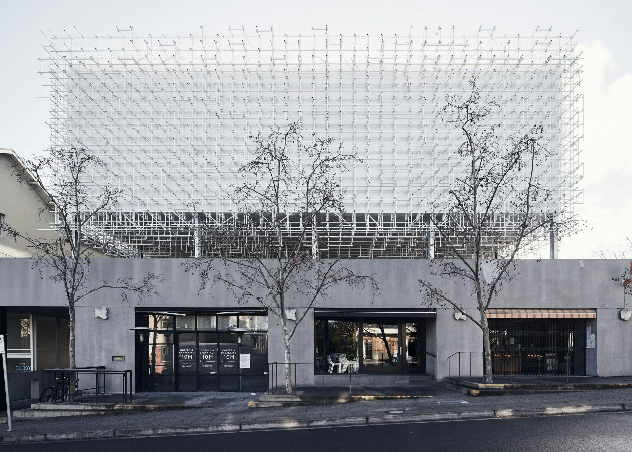 A street view of a grey building with with a big square structure on top.