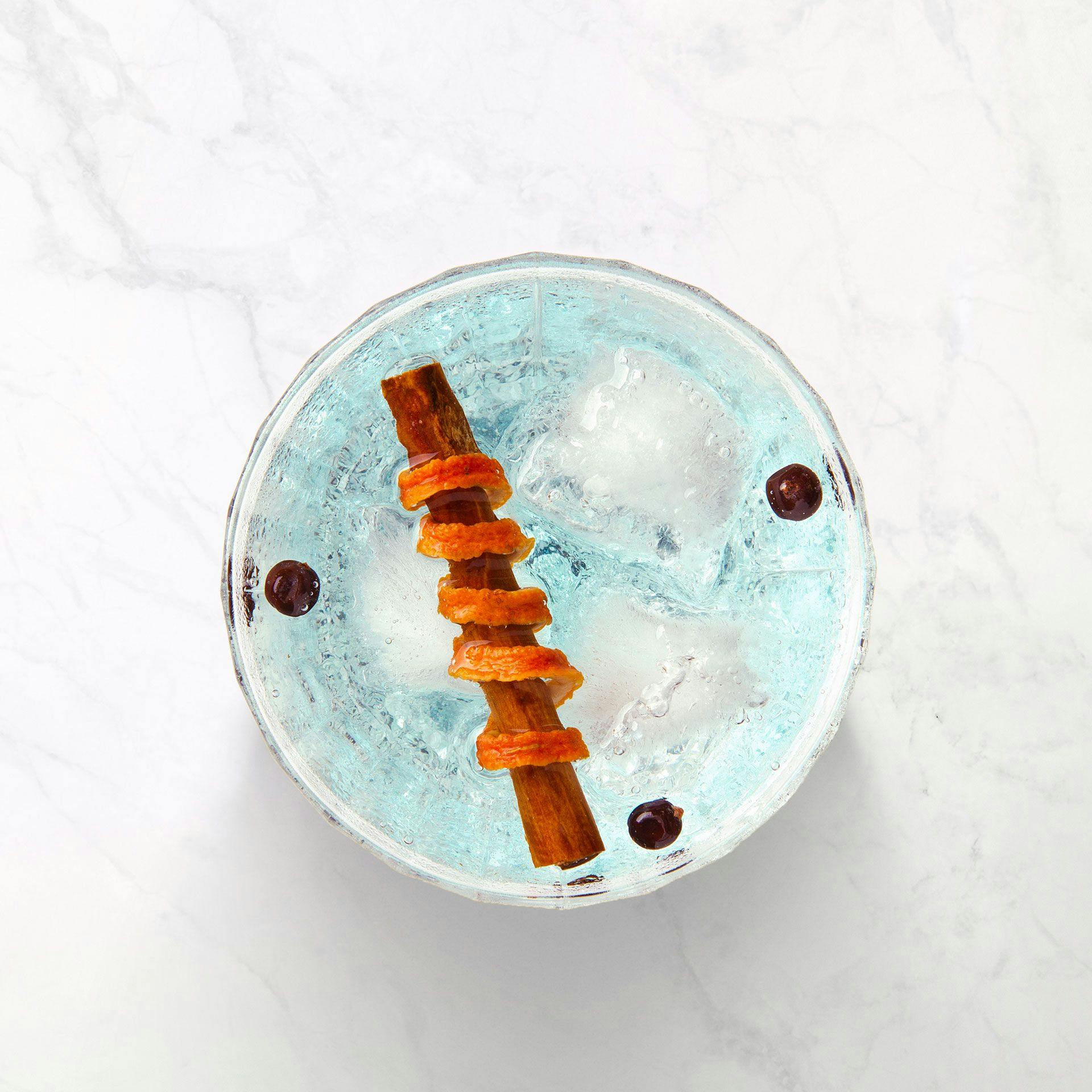 A top view of a clear drink with ice and garnish.