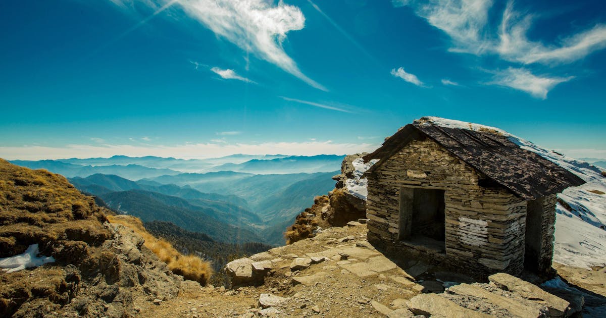 A beautiful house build from stone on the edge of a mountain range. Clouds can be seen covering the mountain ranges in the distance.