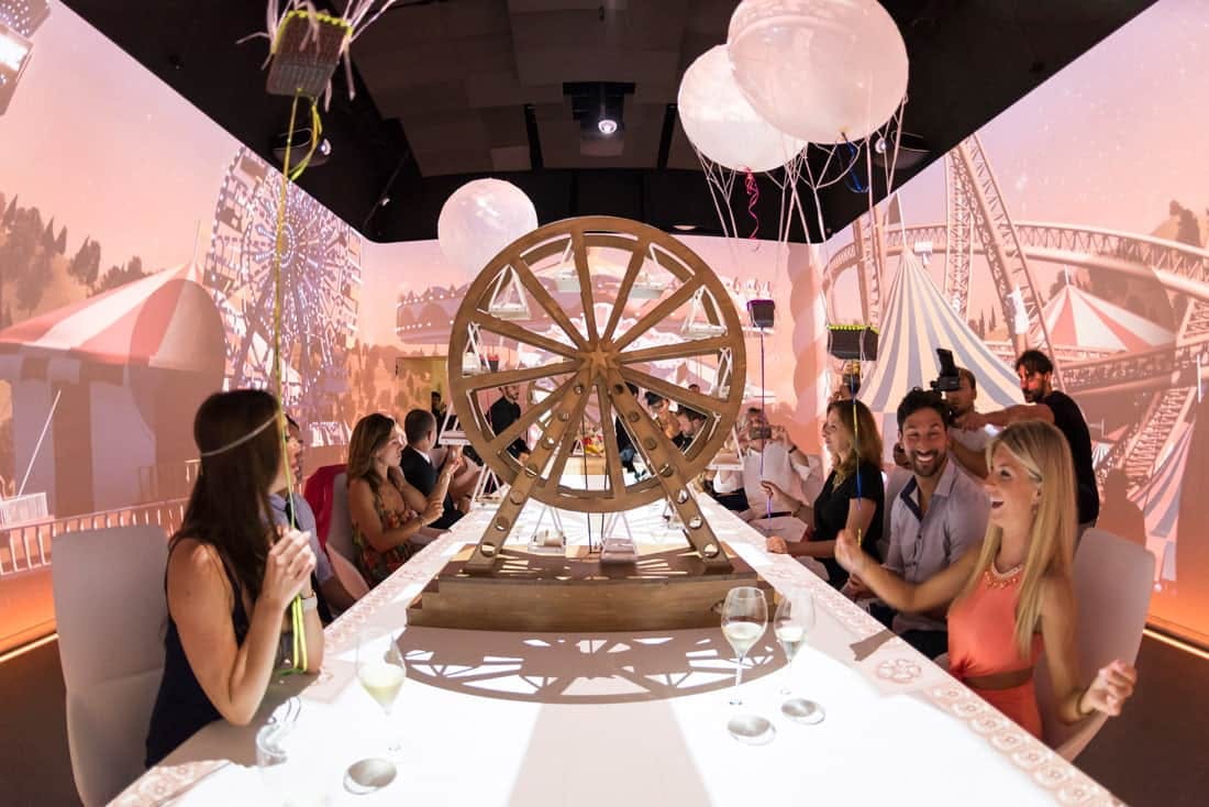 Multiple people sitting at a white table with a round spinning structure on the table.
