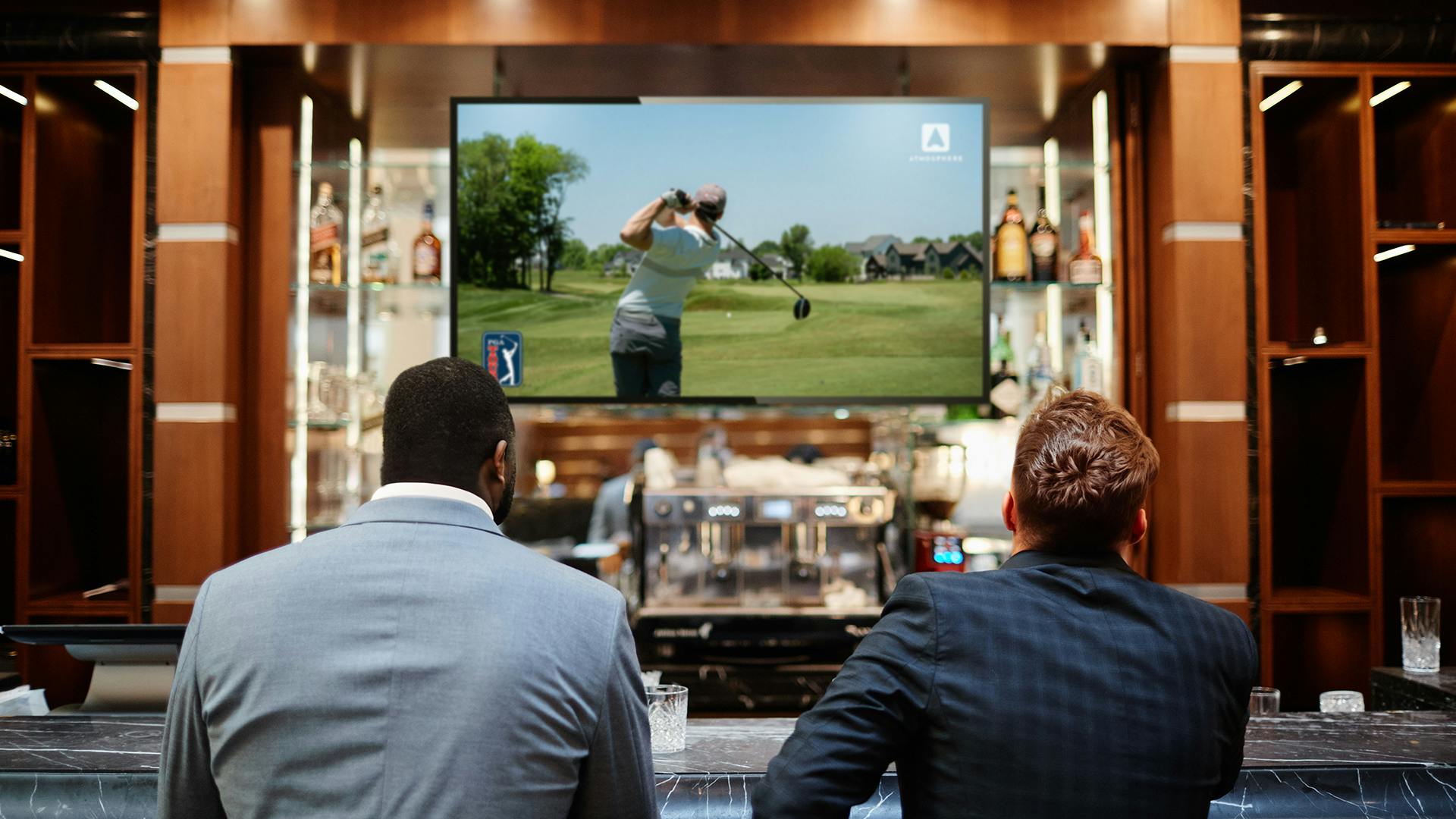 Two men sitting at a bar watching the PGA TOUR channel on Atmosphere TV