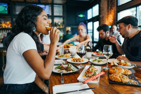 A woman at a table with friends, taking a bite of food.