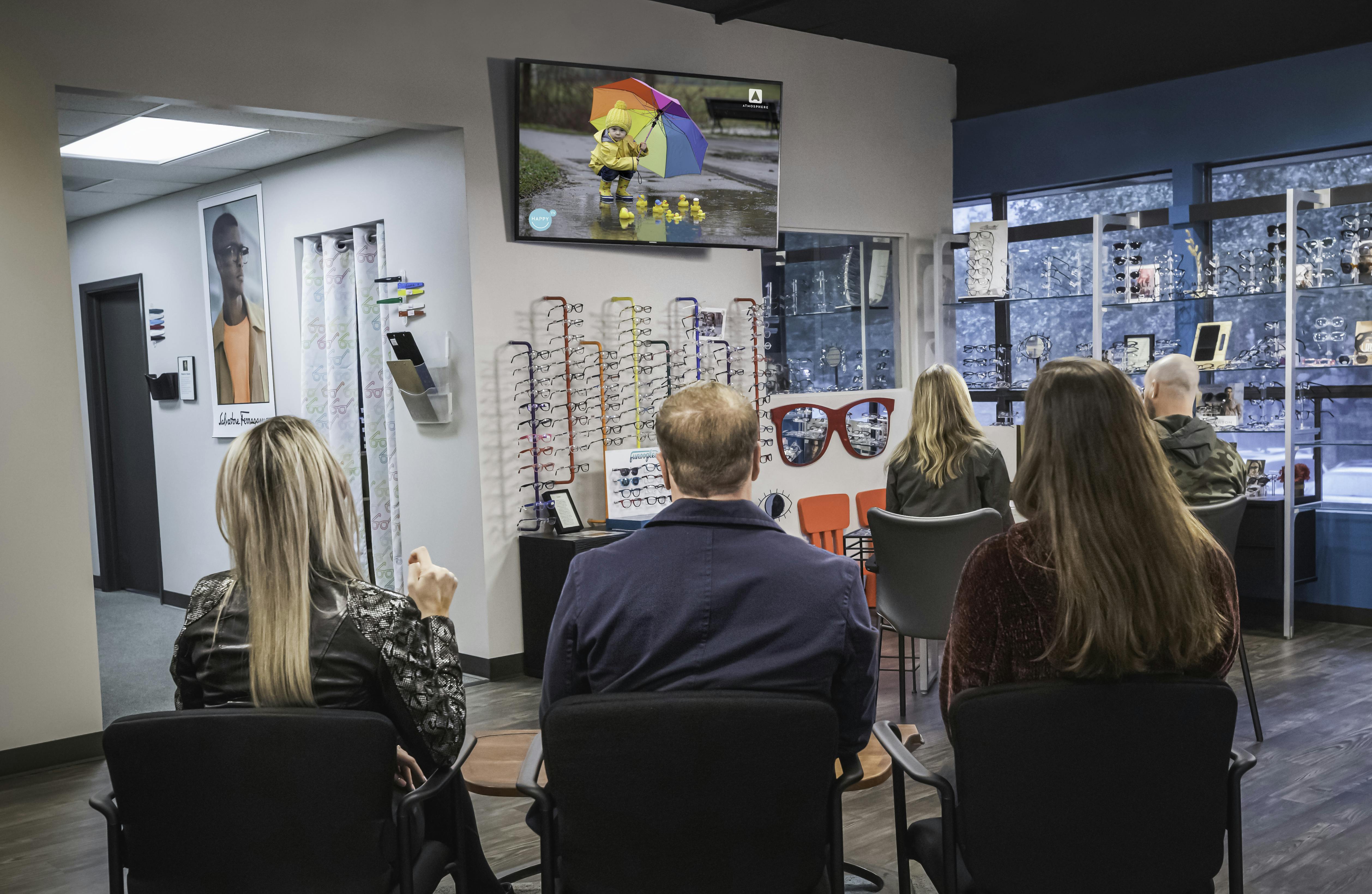 A group of customers watching Atmosphere TV in an eyewear company.