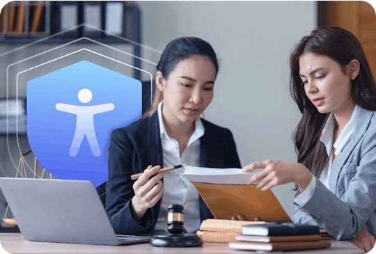 Photo of two female legal experts closely reviewing a document at a desk. An icon of the accessibility man in on a blue shield hovers out of the laptop to represent their guaranteed protection and resources.