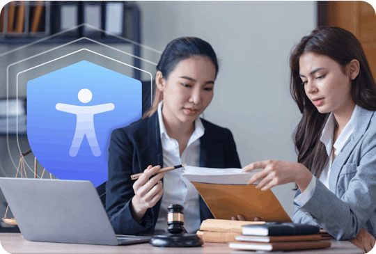 Photo of two female legal experts closely reviewing a document at a desk. An icon of the accessibility man in on a blue shield hovers out of the laptop to represent their guaranteed protection and resources. 