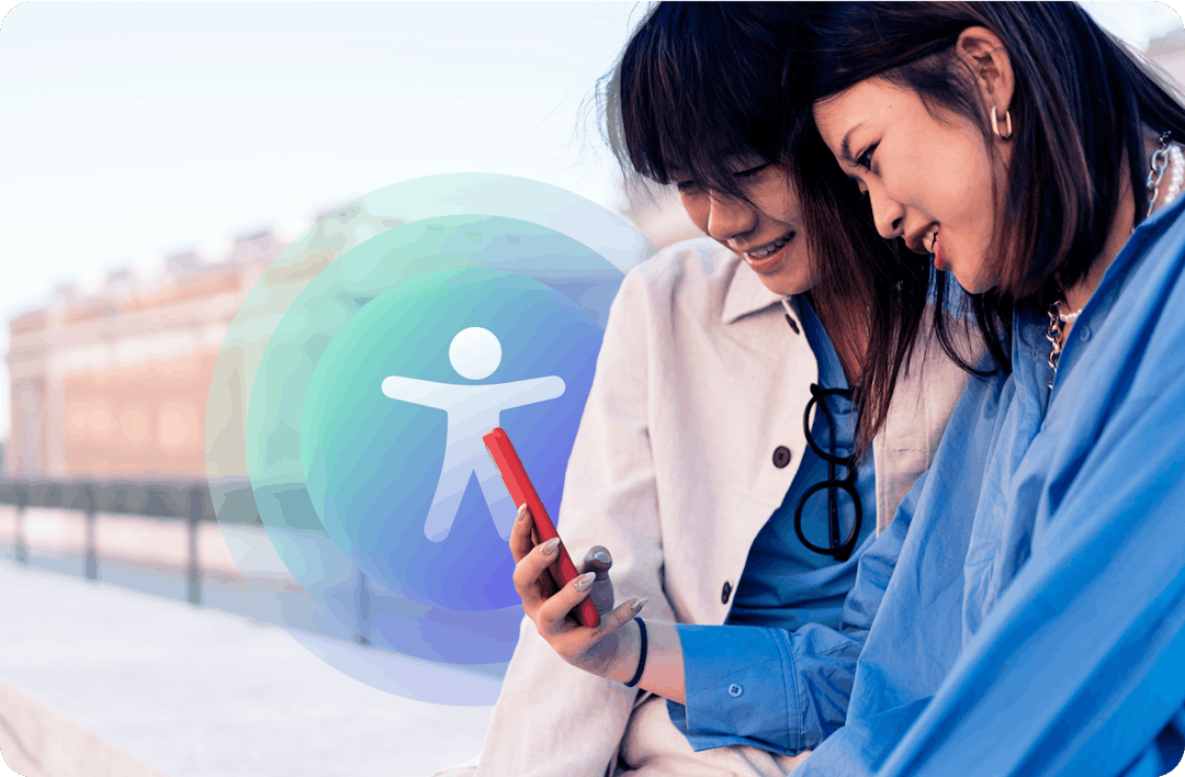 Two asian women looking at a mobile phone with an accessibility symbol behind them