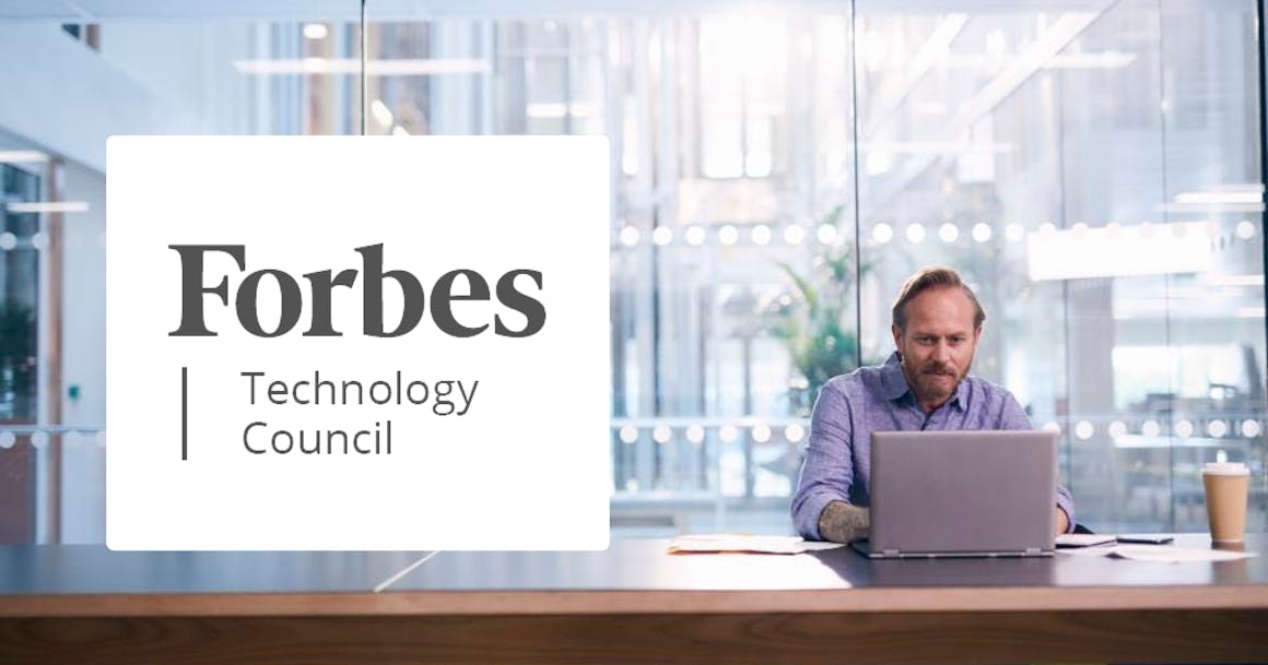 Man sitting at a desk typing on a laptop in front of large glass windows with the Forbes Technology Council logo on top