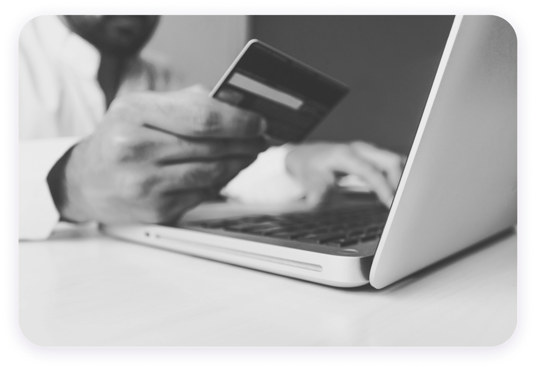 A black man holding a credit card with his right hand and typing on a laptop with his left hand.