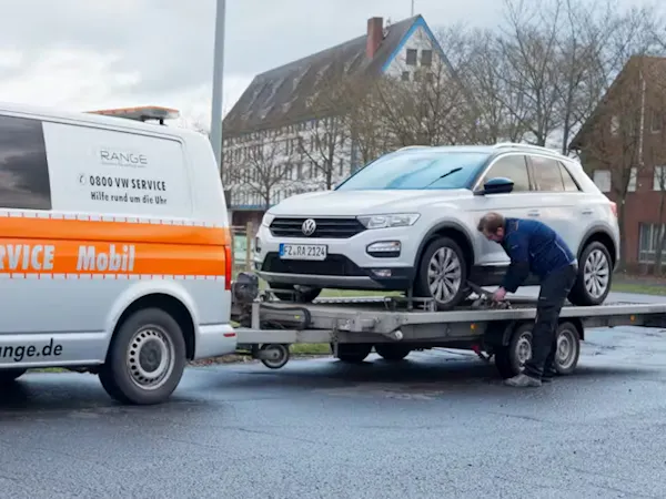 Autohaus Range Service-Mobil-Bus mit Anhänger schleppt einen T-Roc ab.