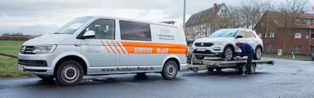 Autohaus Range Service-Mobil-Bus mit Anhänger schleppt einen T-Roc ab.