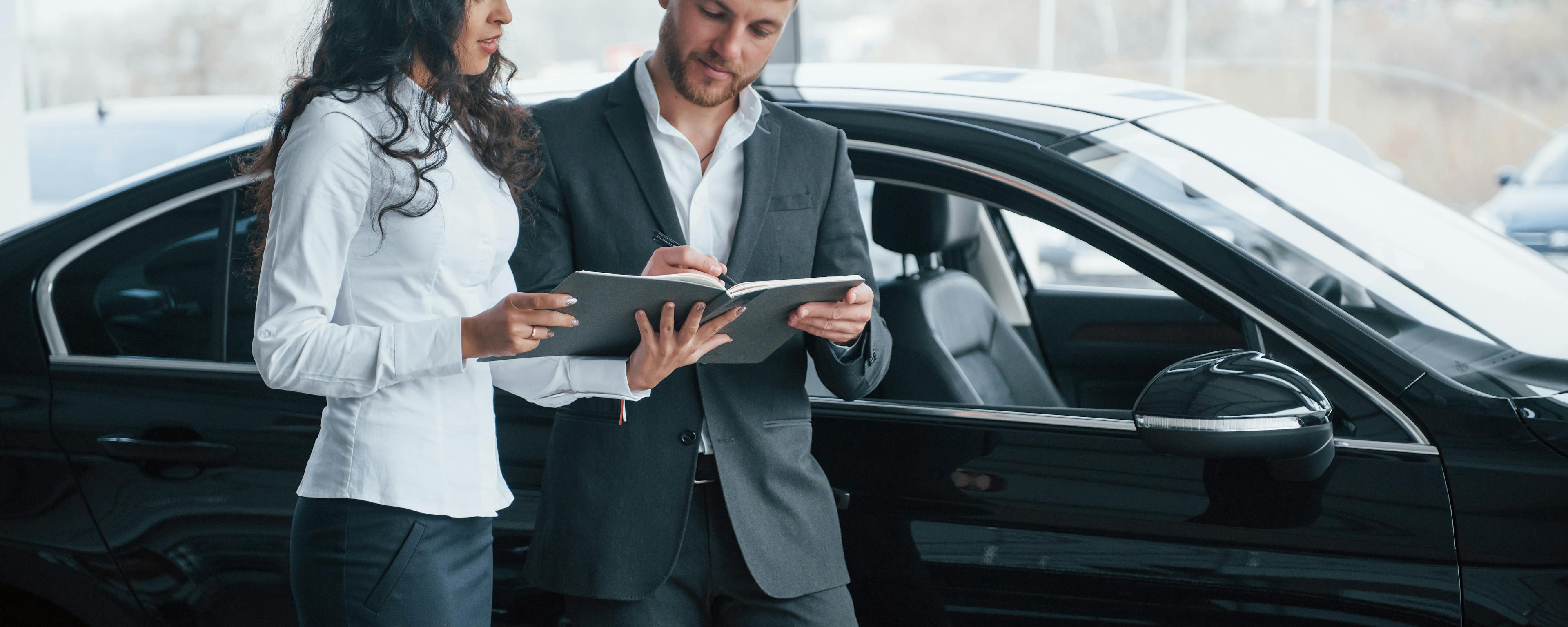 Female Customer Signing Documents of a Male Businessman in Front of a Car