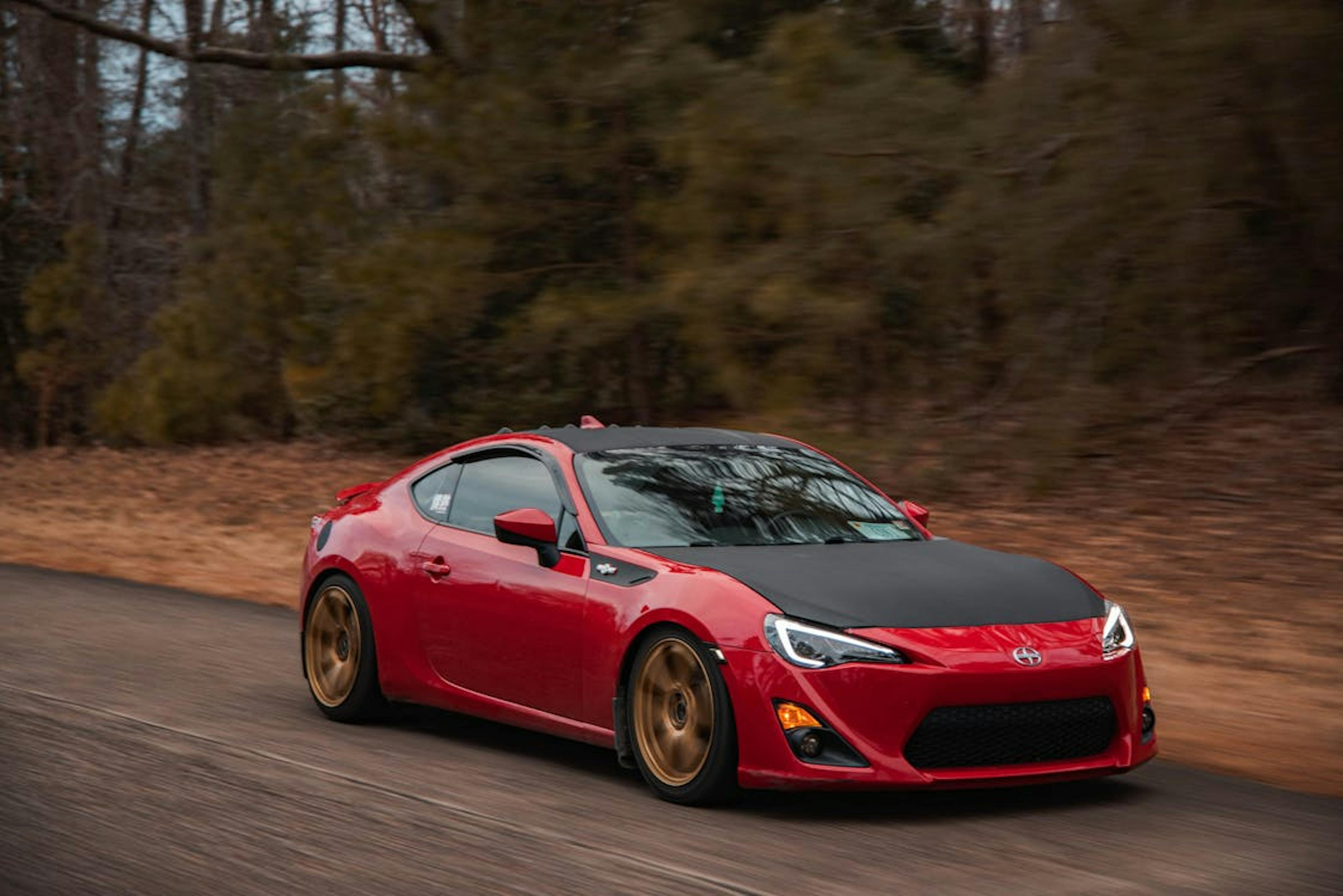 A dynamic image of a stylish red sports car driving fast on a road surrounded by nature.