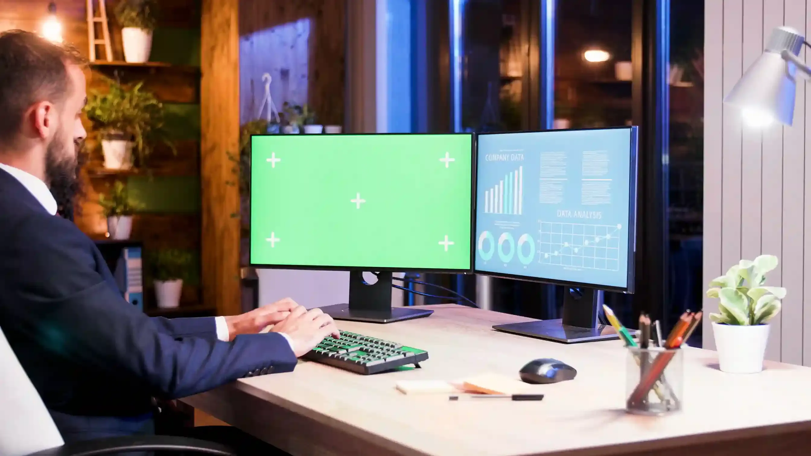 developer working on dual monitors with green screen at night