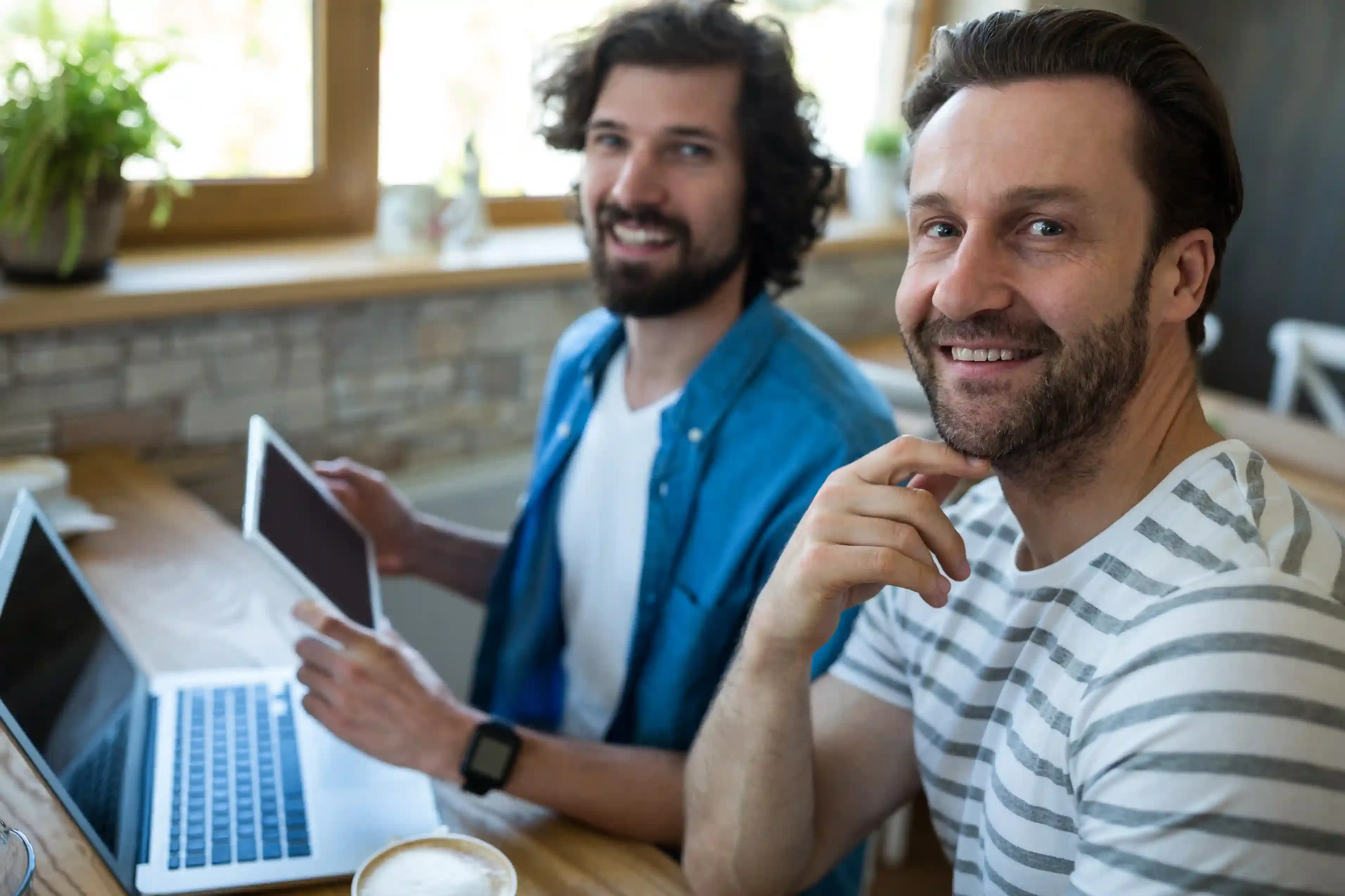 two professionals using tablet and laptop in coffee shop