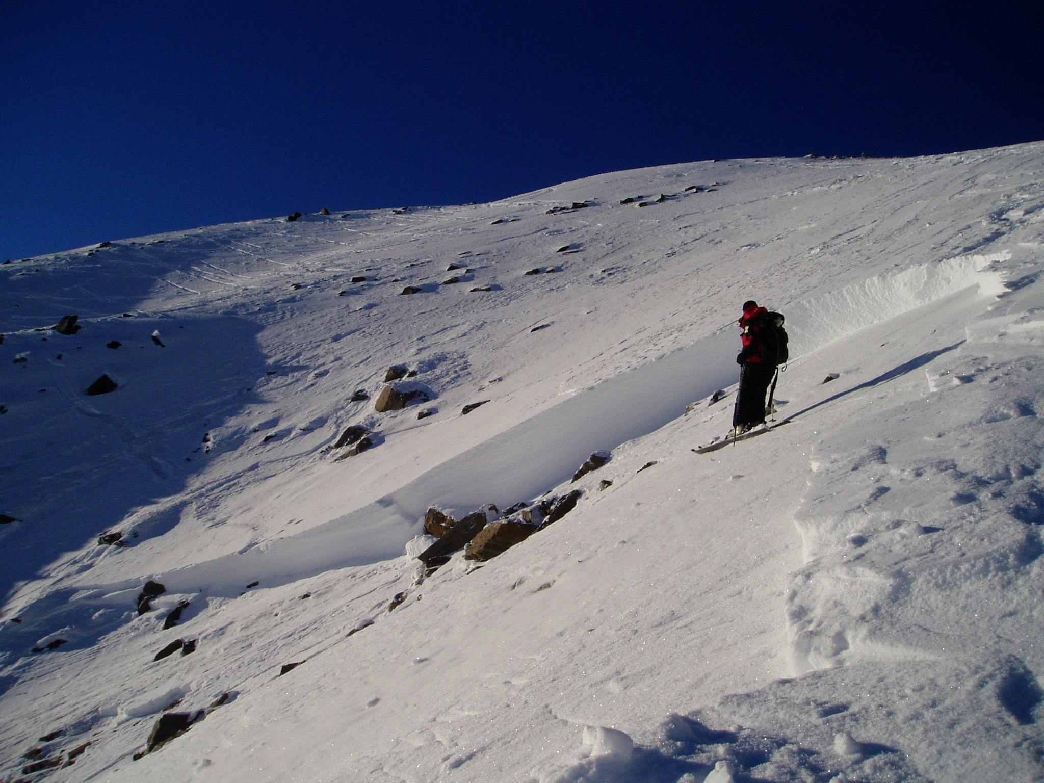 A skier stands near a rock on the bed surface of a slab avalanche.