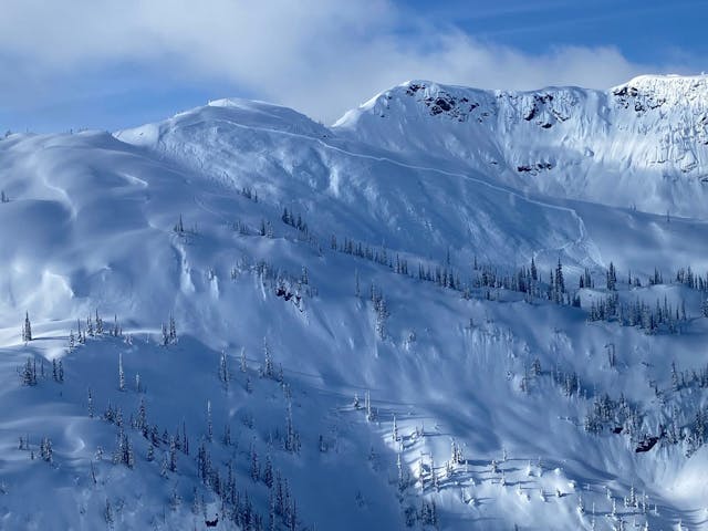 An avalanche propagates widely over an open slope. The image is taken from a distance and the fracture line is prominent even from there. 