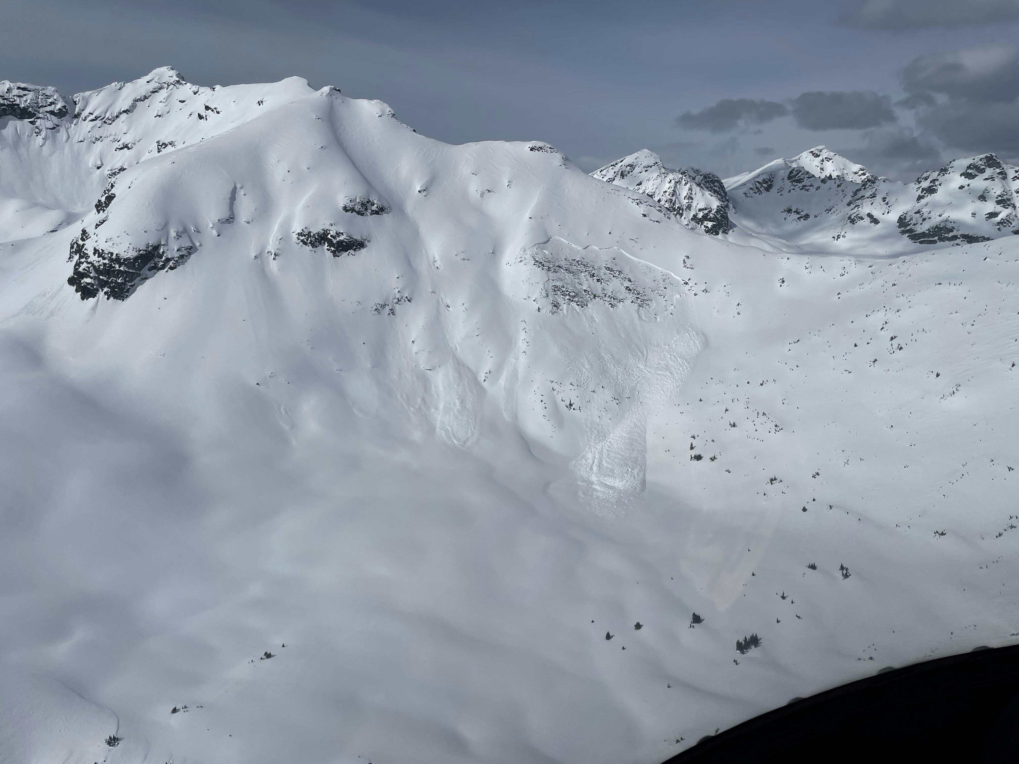 A large avalanche cuts across the face of an alpine slope