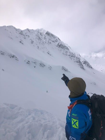 A field team member points up at a rocky area of the mountain