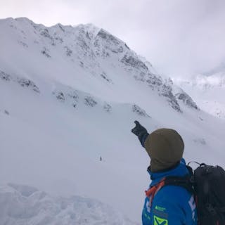 A field team member points up at a rocky area of the mountain